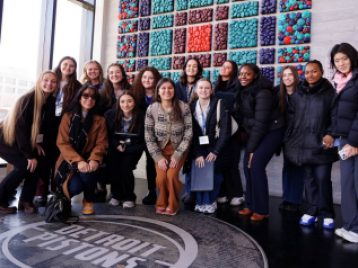 Group of UM students huddled around in the lobby of the Detroit Pistons training center smiling at the camera.